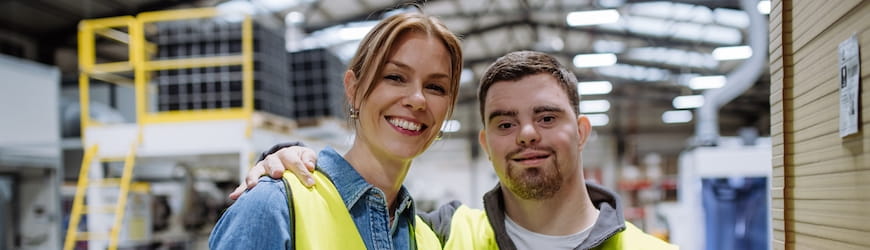 Deux collègues en train de travailler dans un entrepôt logistique, l’un d’eux, trisomique 21, étant en situation de handicap mental. 